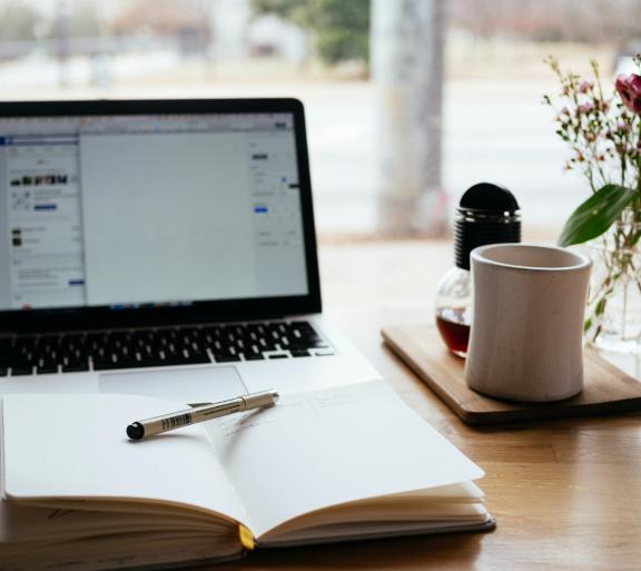 laptop with planner in front and cup of coffee